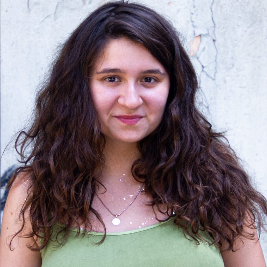 Polina Piddubna is smiling at the camera as her brown hair falls around her. She is wearing a green top.